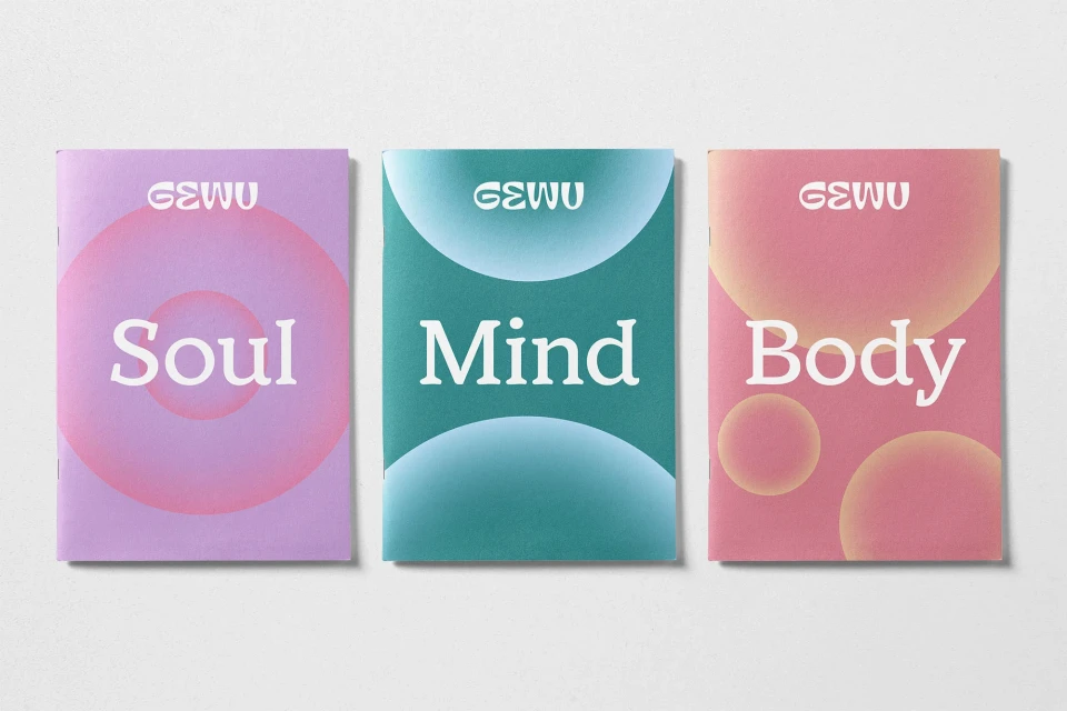 Three vertically-arranged magazines with GEWU logo, pastel colours, and text 'Soul, Mind, Body' against a neutral studio backdrop.