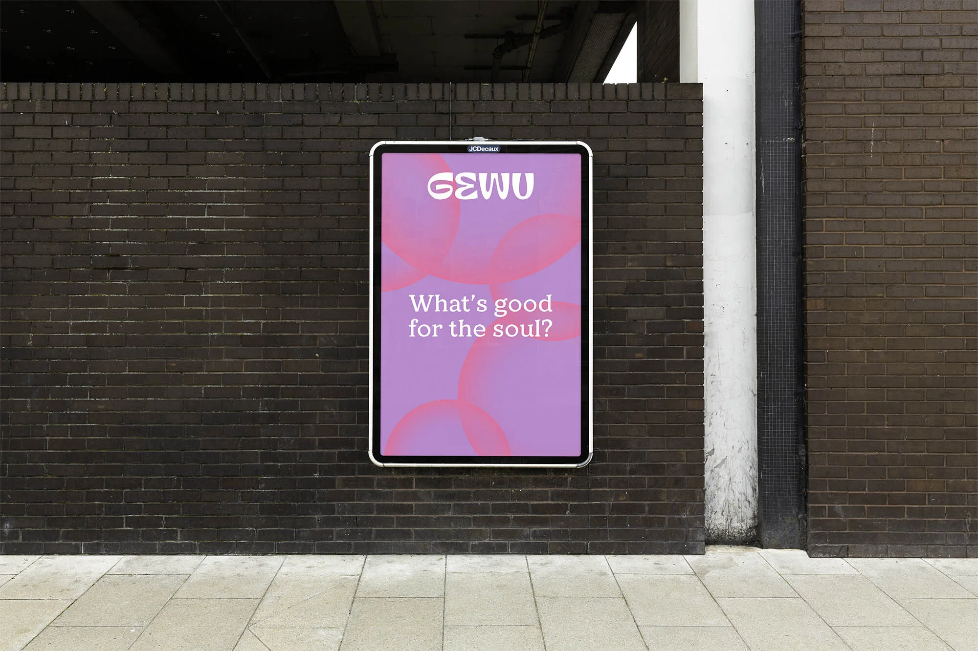 Outdoor advertising billboard on a brick wall features a poster with the text 'What's good for the soul?' and the brand name 'GEWU'.