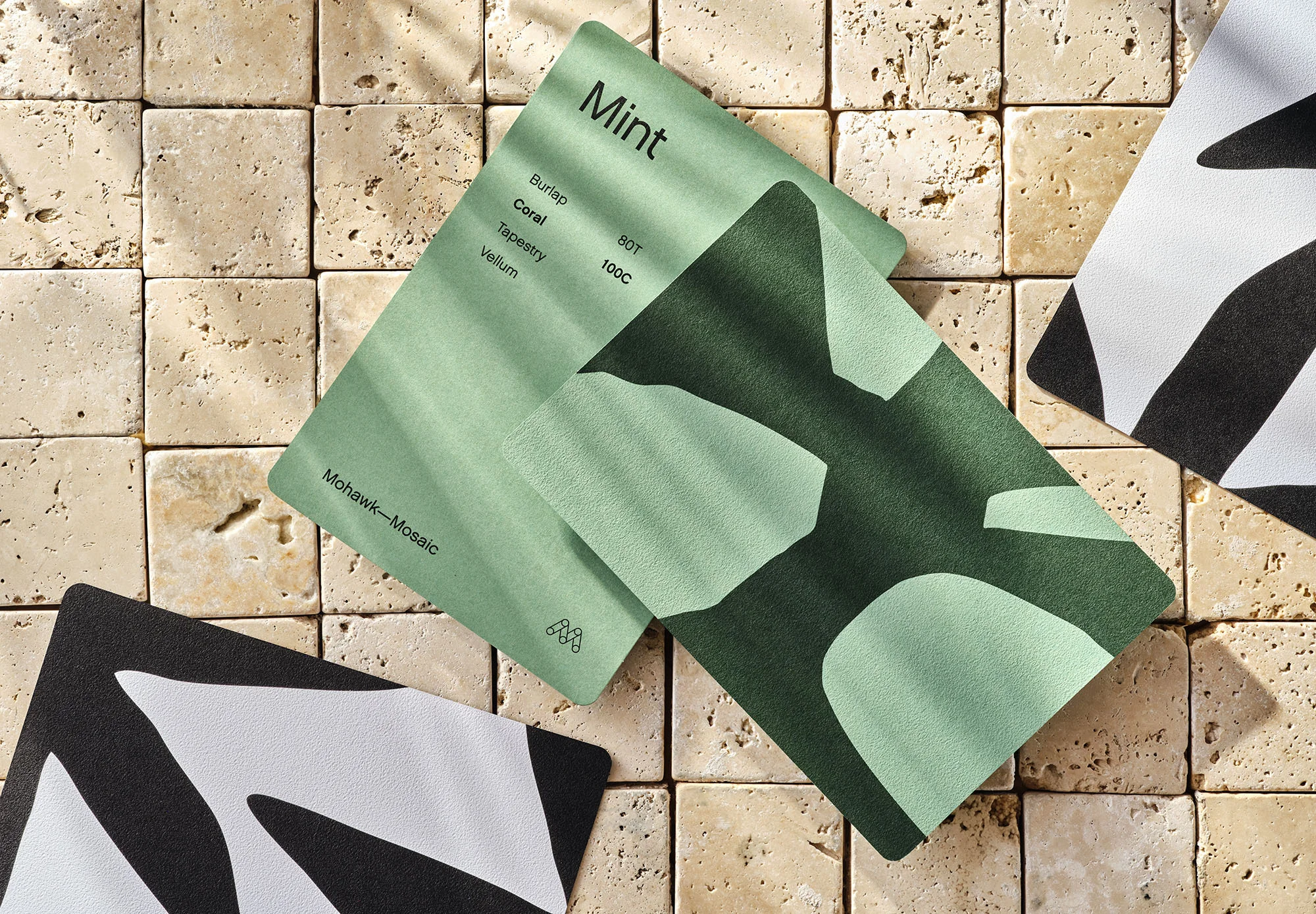 A flat lay of abstract pattern cards in mint, dark green, and black and white on a neutral tile surface with subtle lighting.