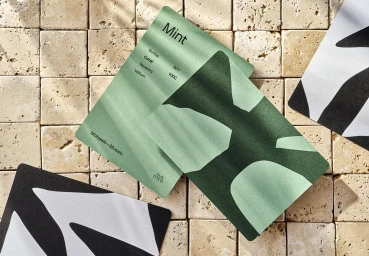 Mint green and black paper sample cards arranged on a travertine stone tile surface with natural light shadows