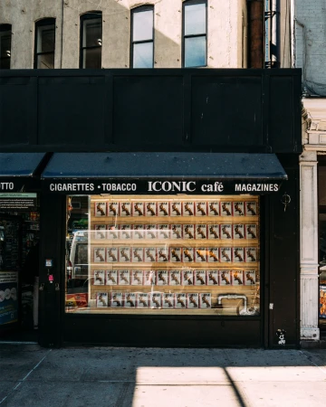 Outdoor shot of an Iconic Cafe displaying magazines in its front window; the building's dark facade stands out against the city street.