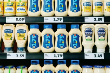 Supermarket shelves stocked with various brands of mayonnaise bottles and pricing labels.