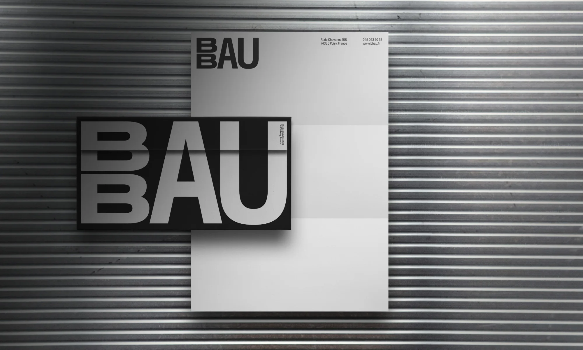 Graphic design featuring the word 'BAU' in bold typography, layered on a white board against a textured grey corrugated metal backdrop.