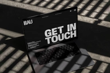 A laptop computer displaying a dark website design with bold white text reading GET IN TOUCH on a textured surface.