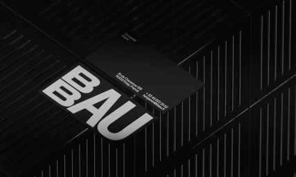Monochrome product shot of BBAU brand identity featuring black business cards and bold typography resting on a dark ribbed surface