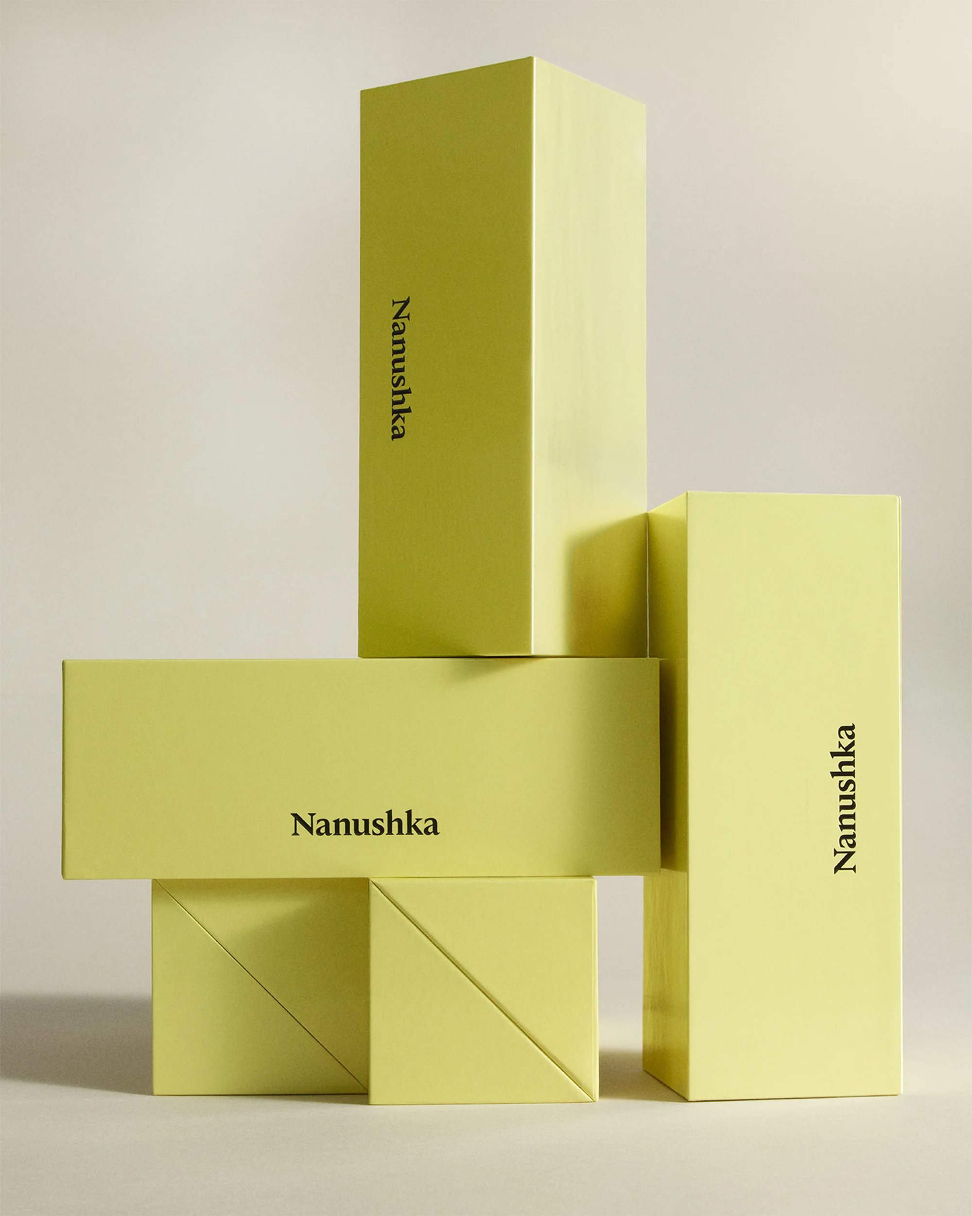 Stacked Nanushka brand boxes in various sizes and orientations against a neutral backdrop, arranged in a visually appealing composition.