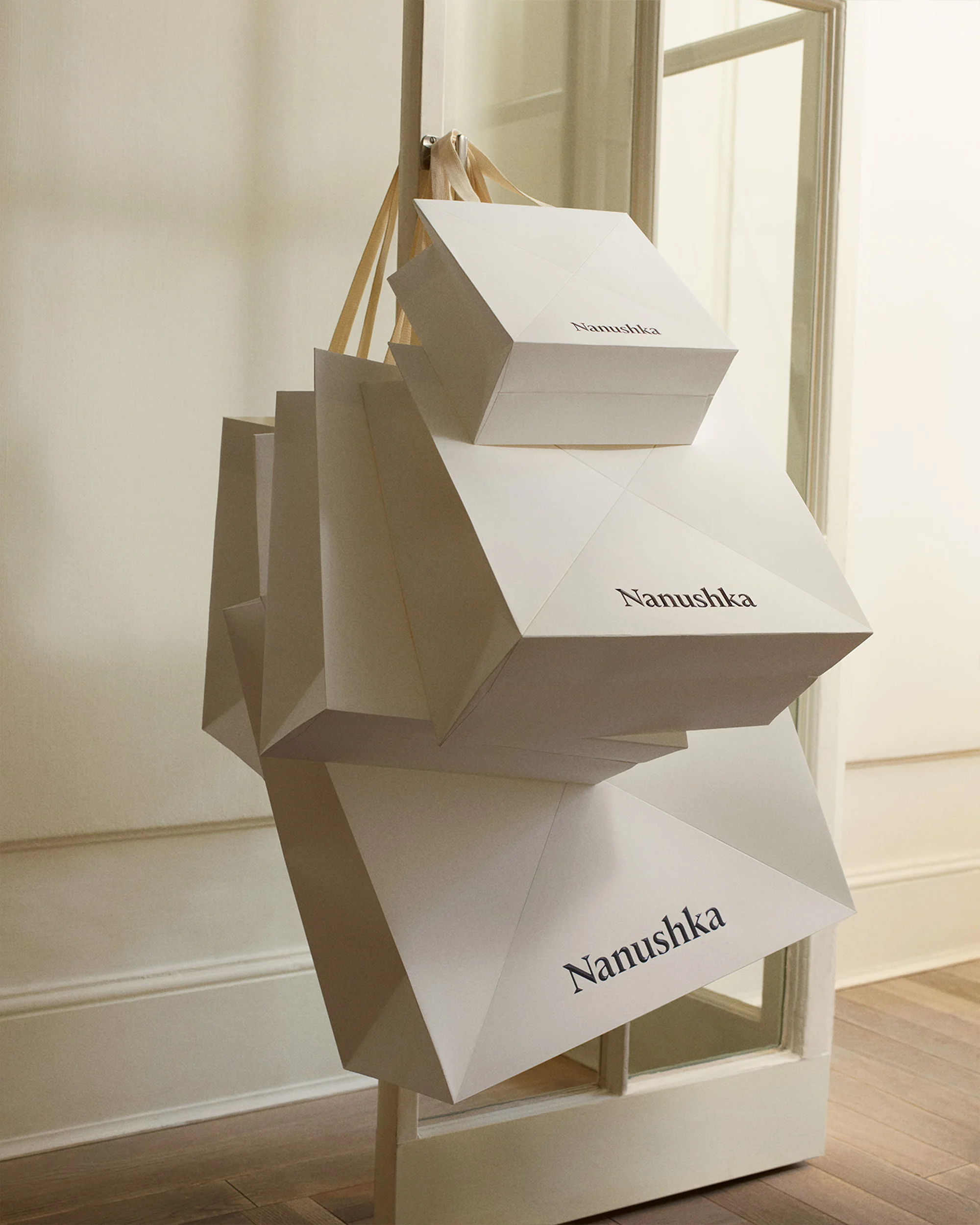 Multiple white Nanushka shopping bags hanging on a rack near an open doorway, simple elegant design in a neutral color palette.