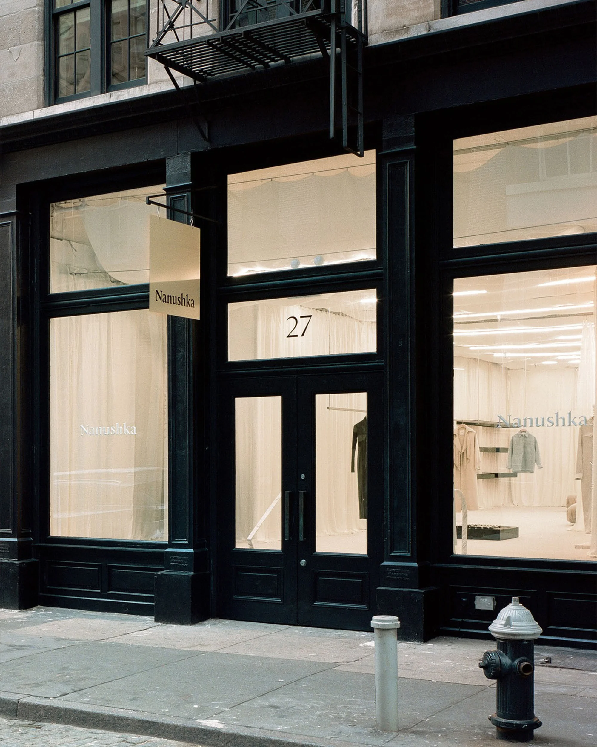 Exterior of the Nanushka store, with a black facade, large windows, and an awning. The storefront is captured in a neutral daytime setting.