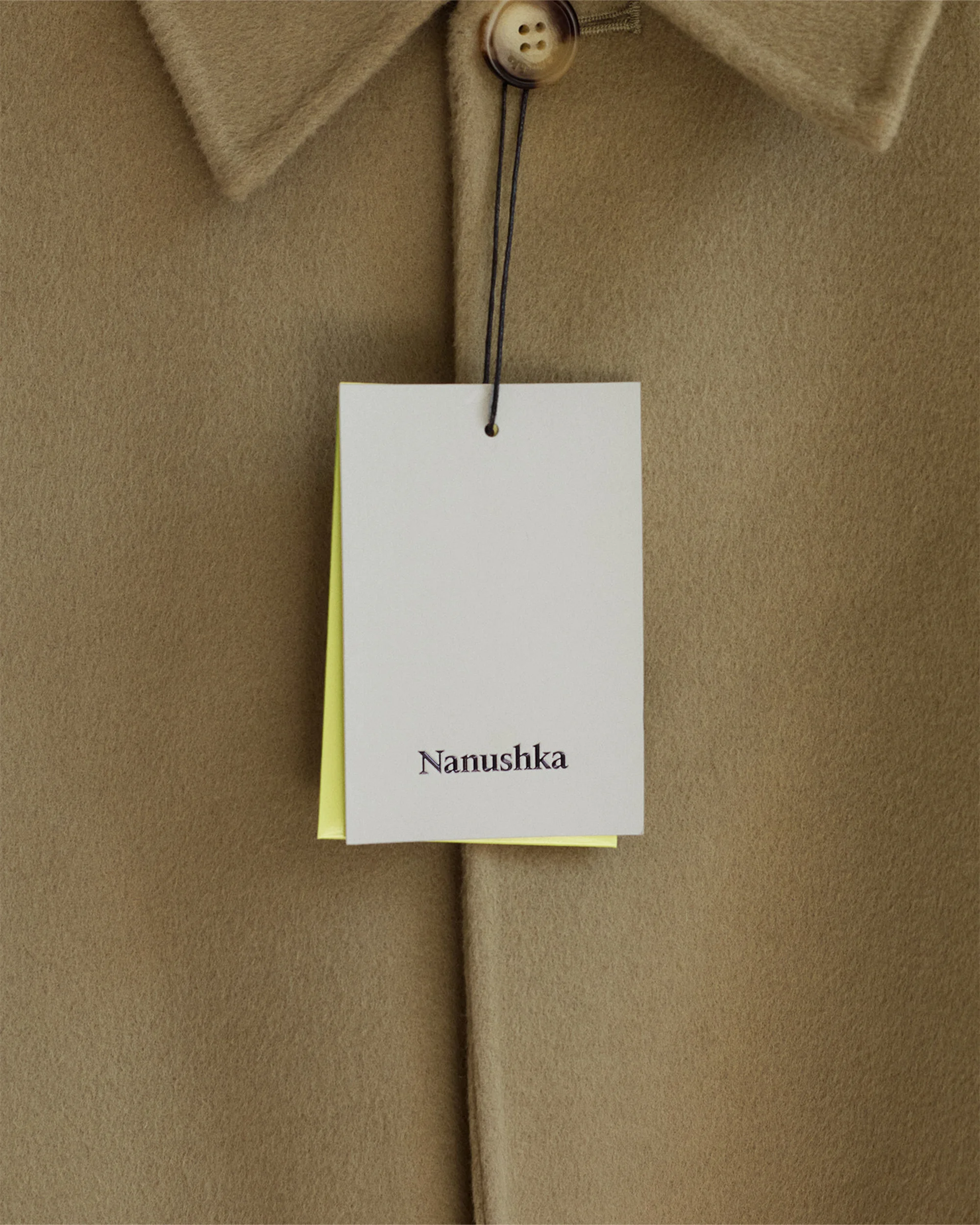 Close-up of a beige Nanushka collared coat with a button and a brand tag, showcasing fashion and design in a studio setting.