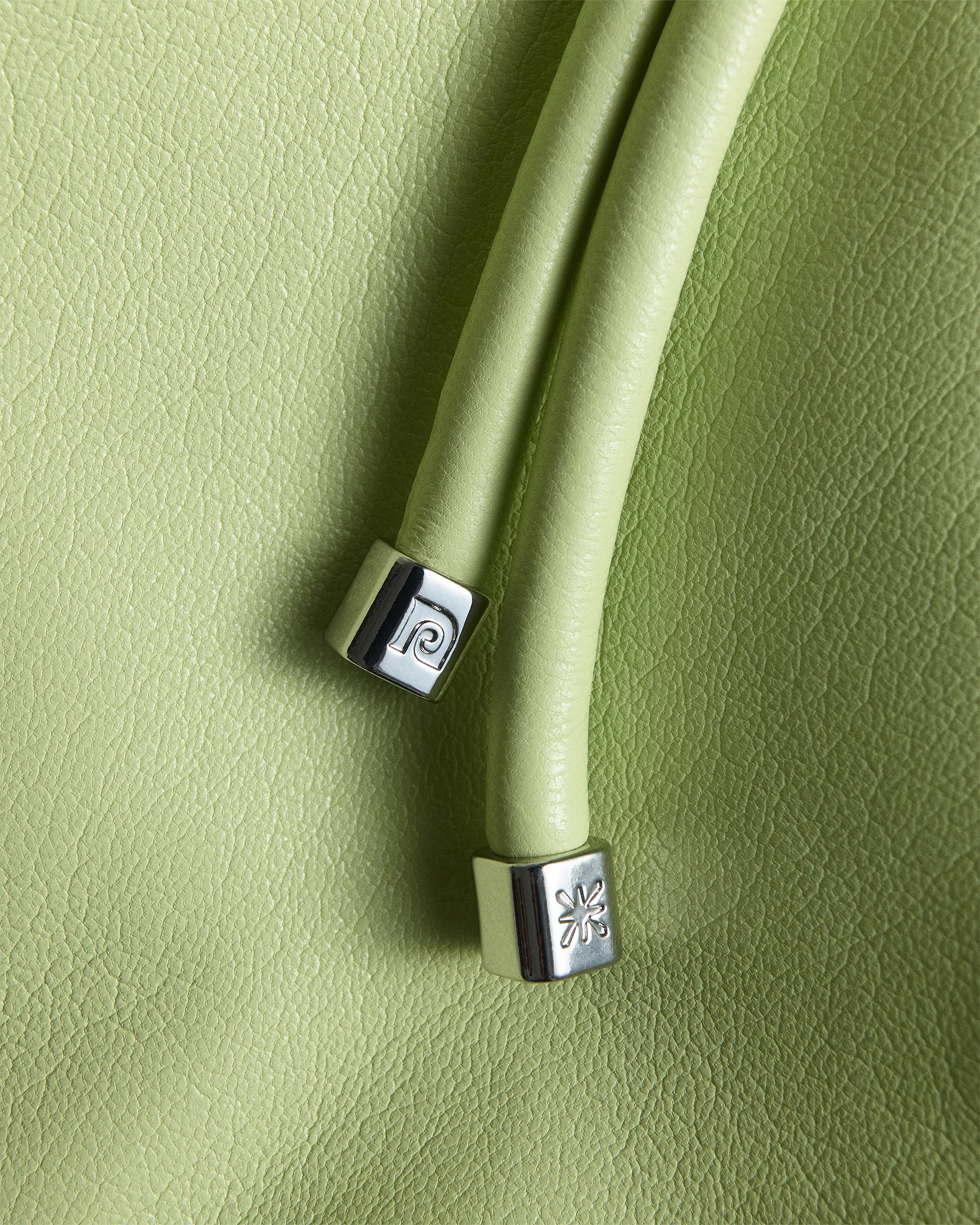 Close-up of a light green leather handbag with two rounded handles, each capped with silver hardware featuring designer logo imprints.