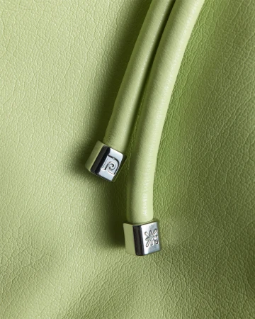 Close-up of a light green leather handbag with two rounded handles, each capped with silver hardware featuring designer logo imprints.