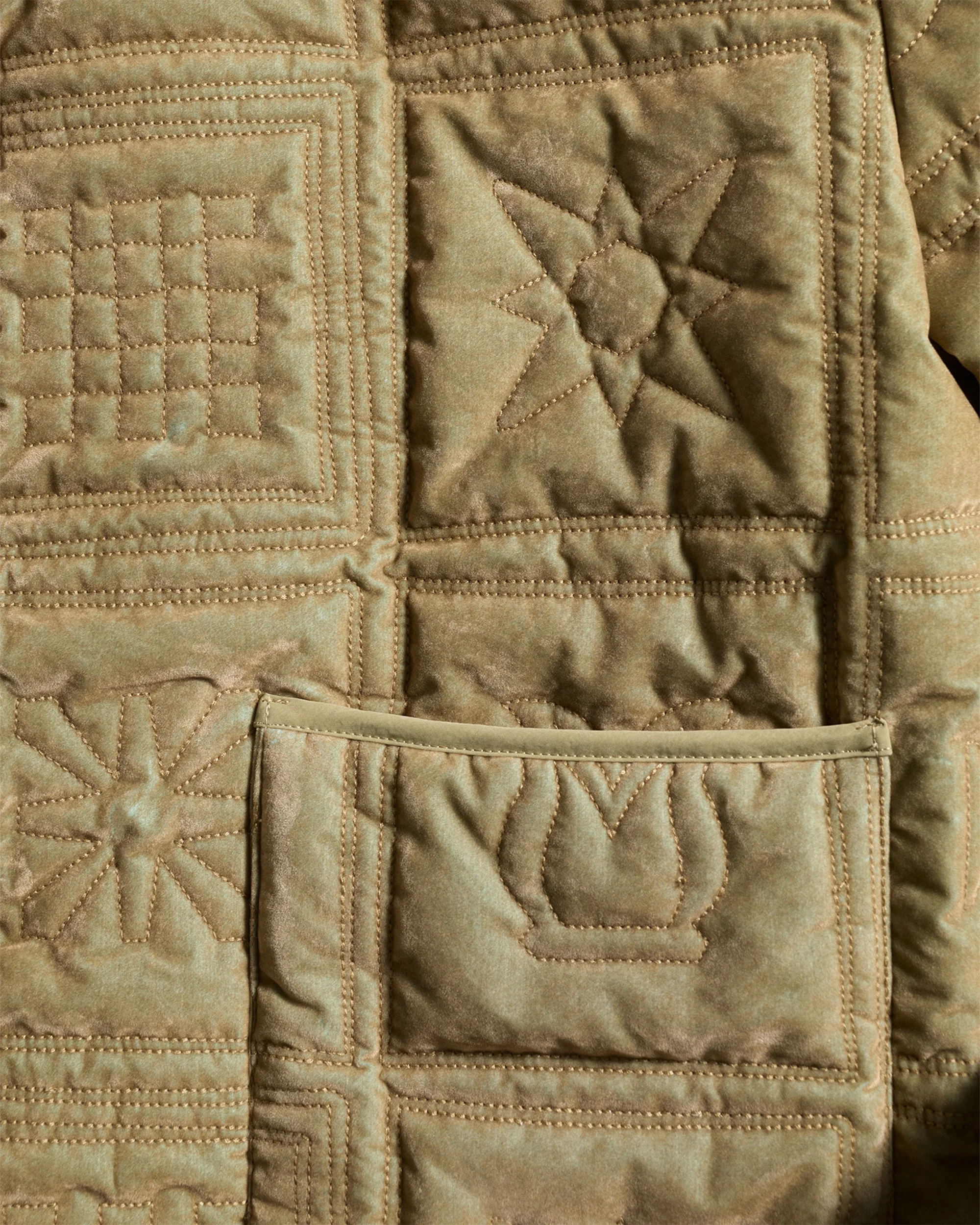 Close-up of a tan quilted jacket with geometric stitching and a pocket, showcasing textile patterns and fashion details.