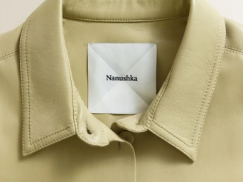 Close-up of a pale green leather jacket collar with a branded clothing tag reading Nanushka inside the neckline.