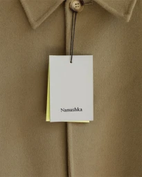 Close-up of a Nanushka clothing tag hanging from a camel-colored wool coat button by a black string