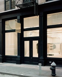 Exterior storefront of the Nanushka retail store with dark framed glass windows, a hanging sign, and the number 27 above the double doors.