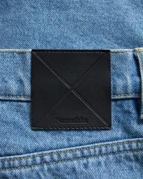 Close-up of a black leather brand patch stitched onto blue denim jeans with contrast yellow topstitching.