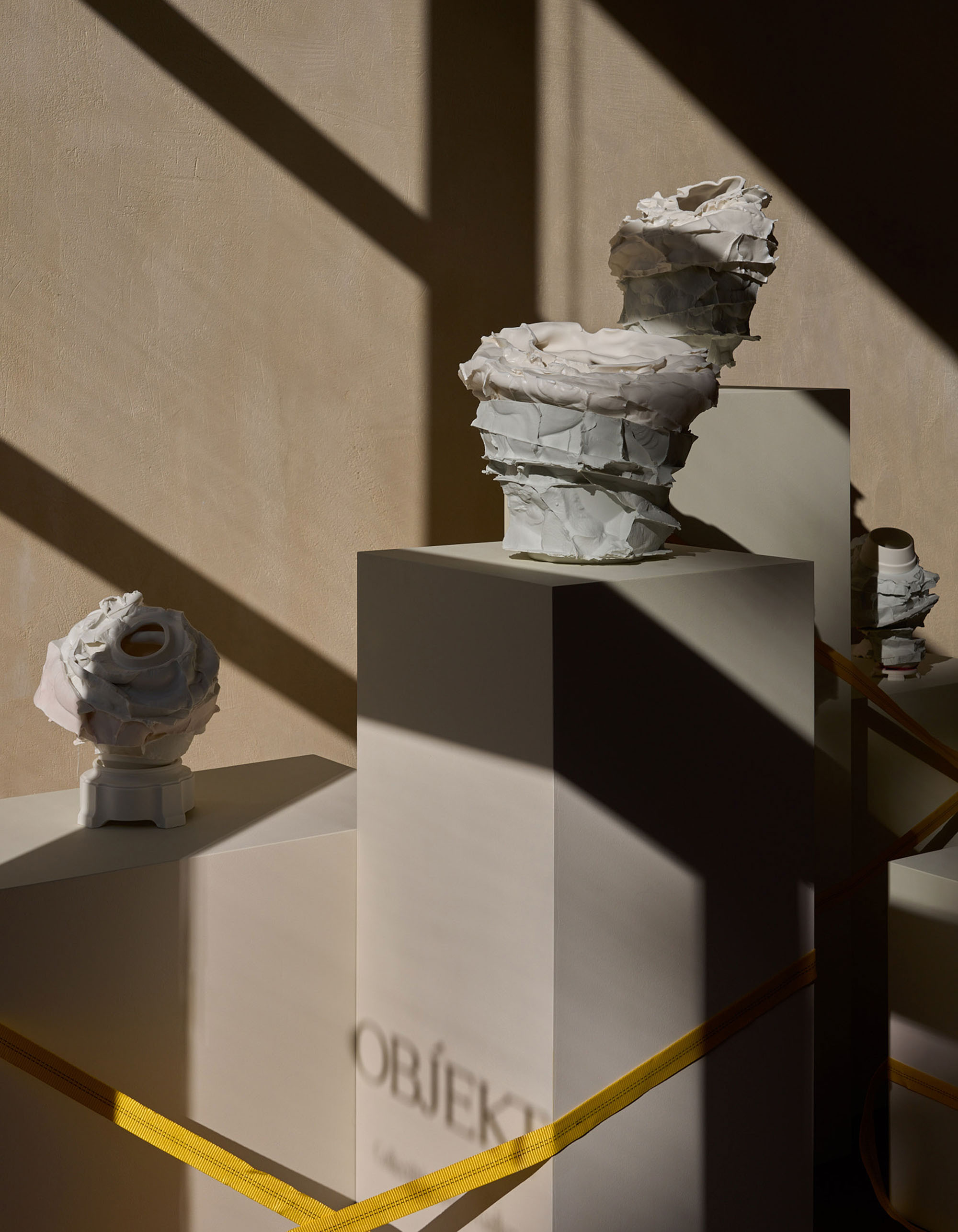 Art installation featuring two abstract white sculptures on pedestals, bathed in light and shadow in an indoor environment.