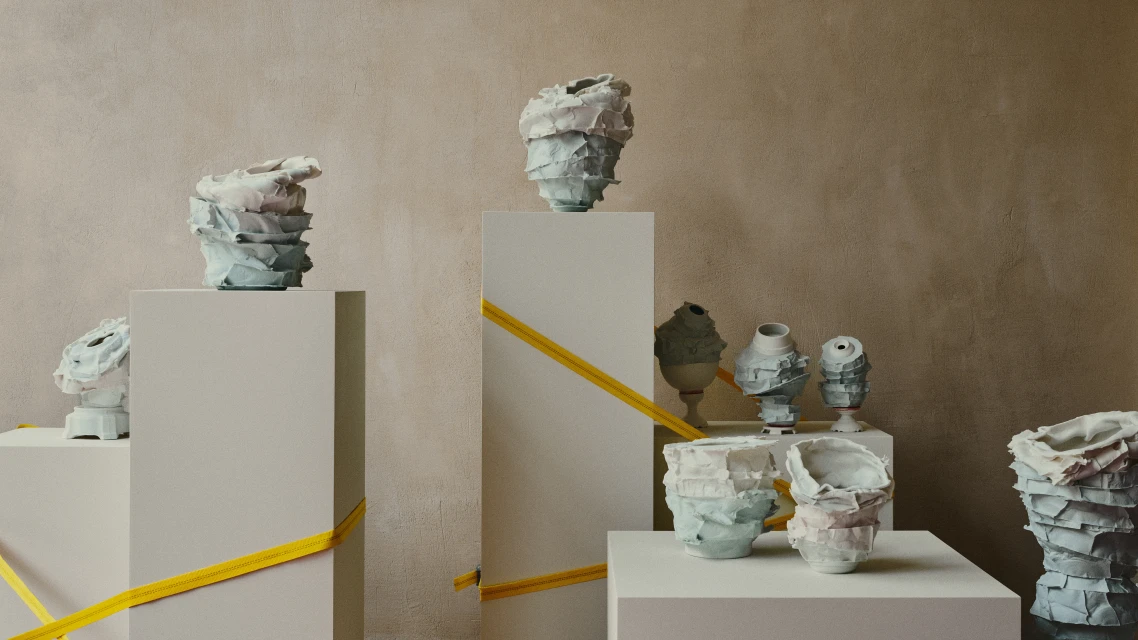 Collection of handcrafted ceramic vases displayed on pedestals with geometric ribbon accents against a neutral-toned wall, creating an artful exhibition.