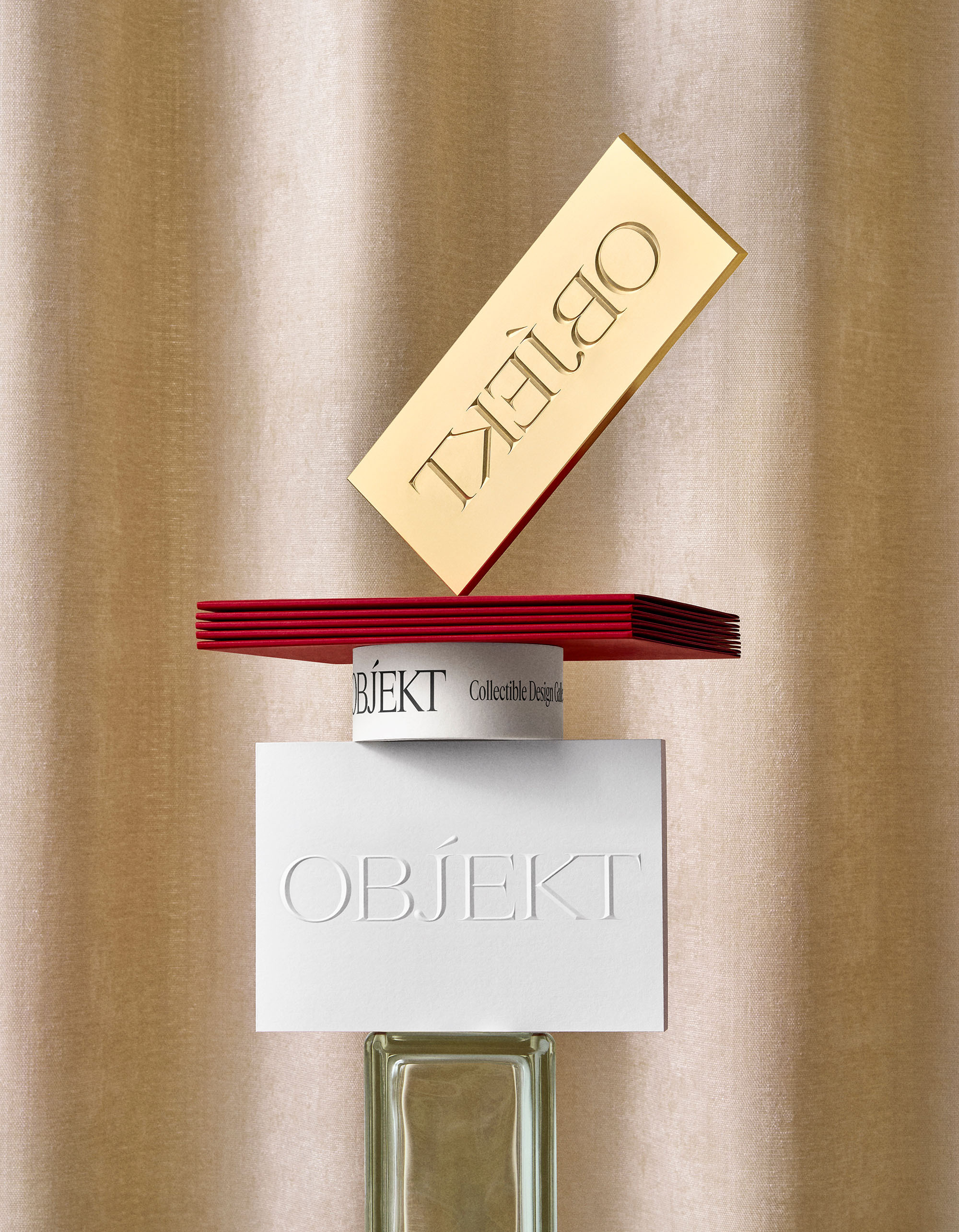 Still life of geometrically-arranged 'Objekt' branded cards and block, with red, white, and gold colors against gold backdrop.
