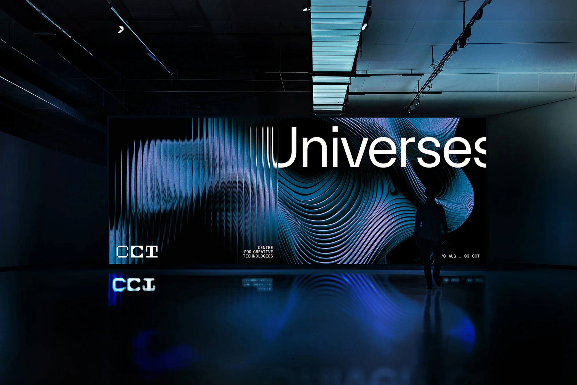 Silhouetted figure stands before a digital art installation featuring vibrant abstract patterns and the word 'Universes' in a dark room.