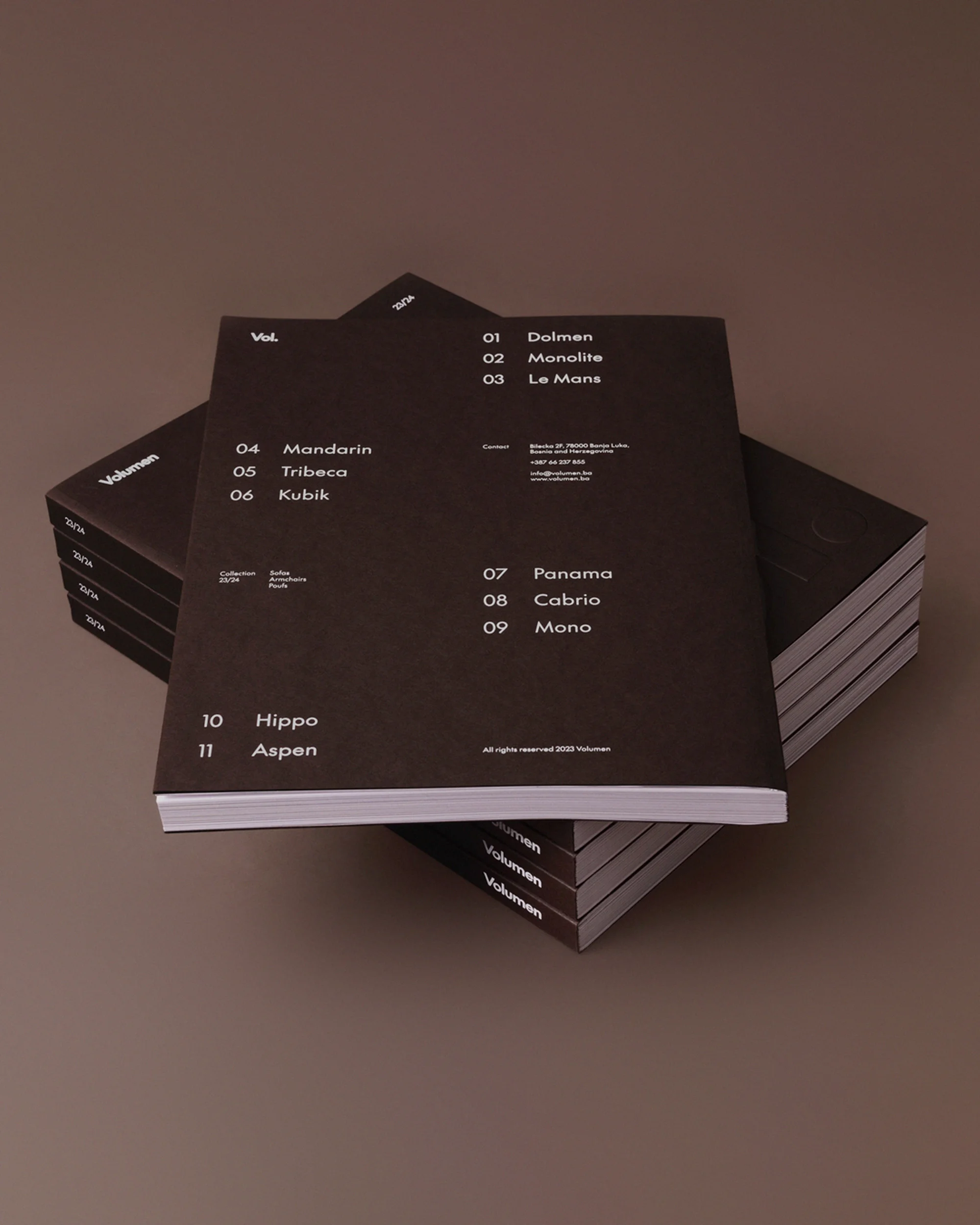 Stack of Volmen books with black covers and white text arranged on a plain brown background, showcasing minimalist design and typography.