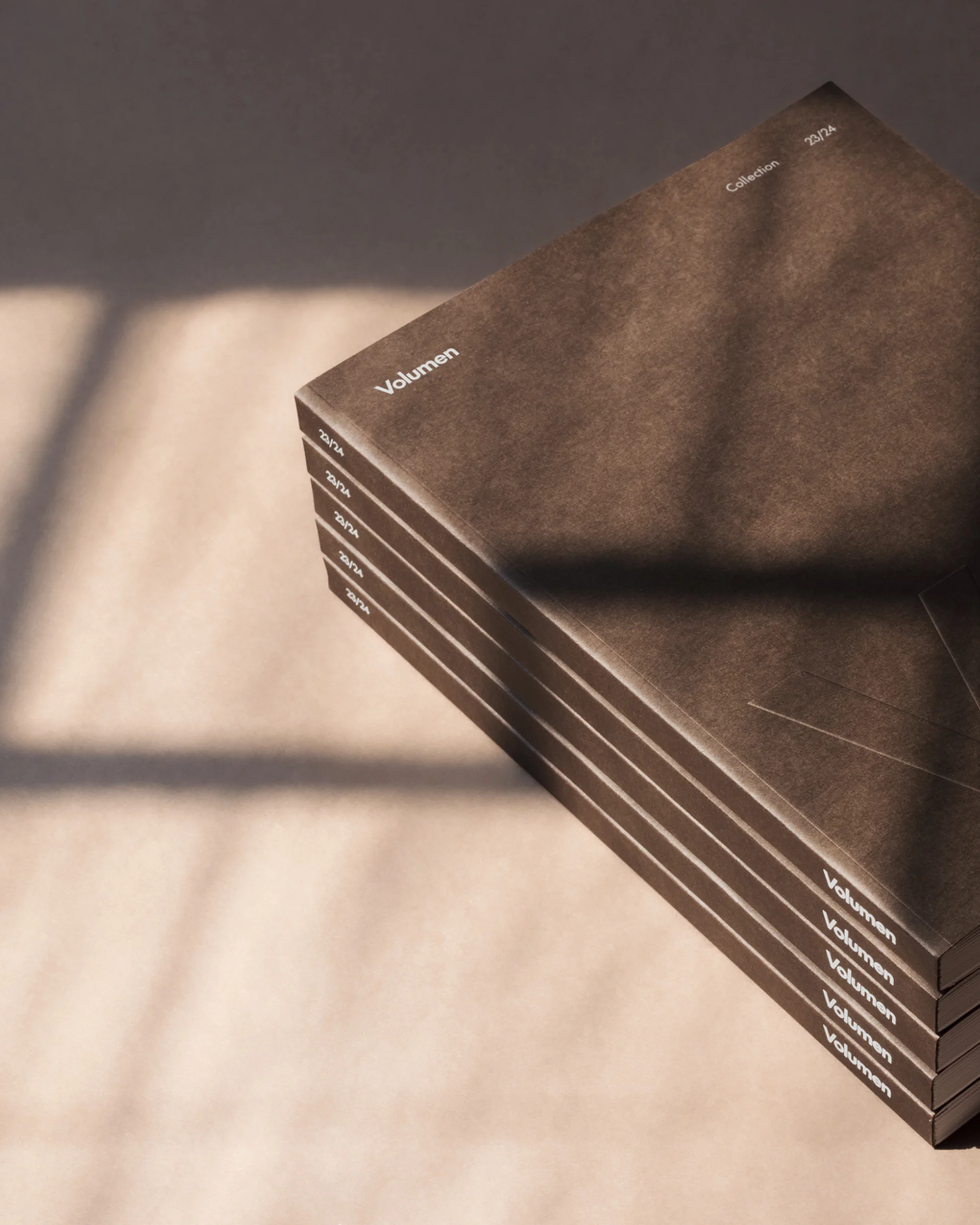 Stack of brown-covered Volumen collection books with a light ray casting a shadow, perfect for graphic design or book design inspiration.