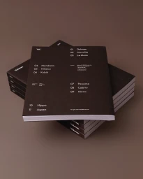 A stack of dark brown booklets with minimal white typography resting on a brown surface