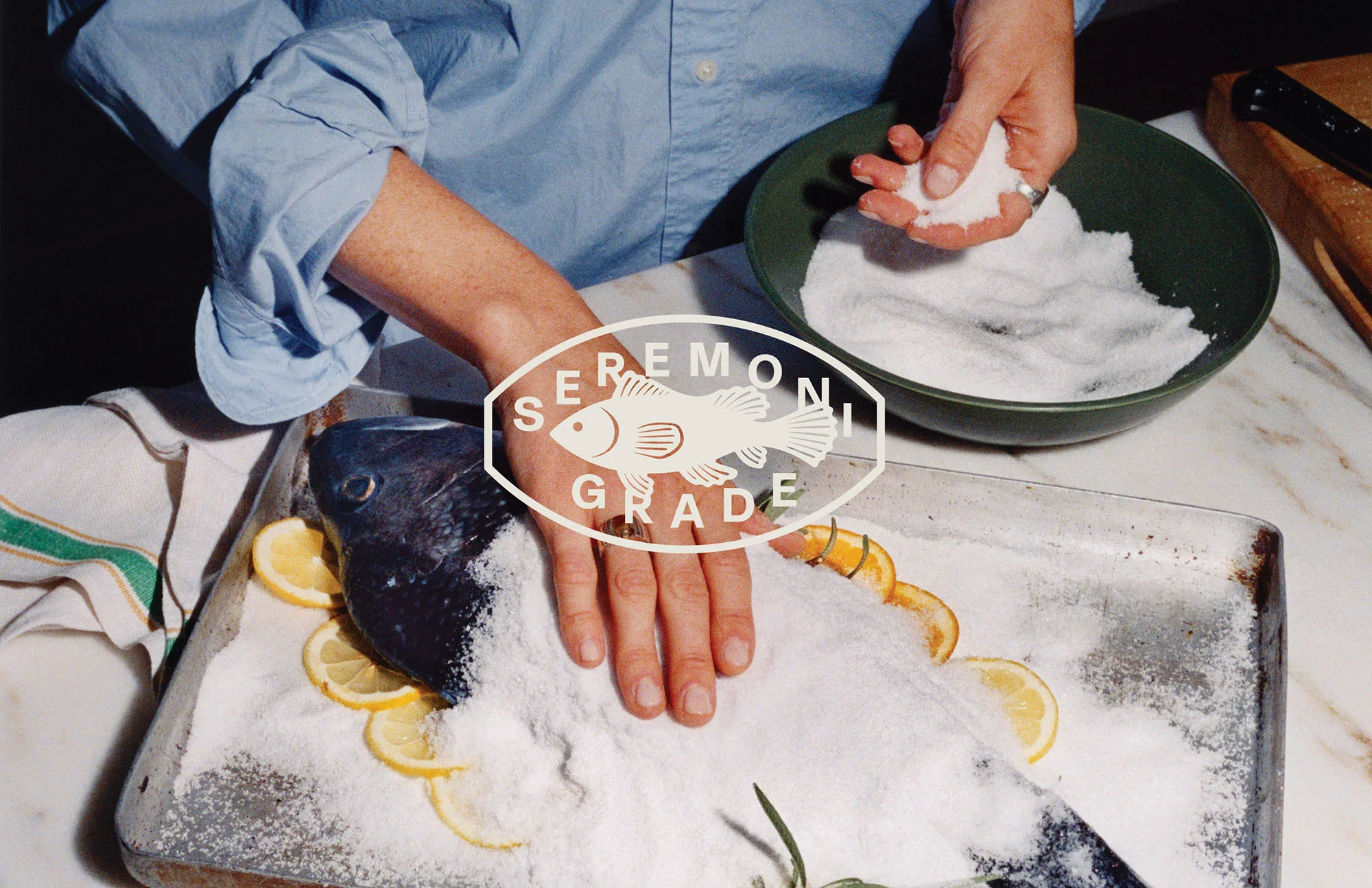 Overhead shot of a person preparing salt-baked fish with lemon slices, showcasing culinary art and food preparation.