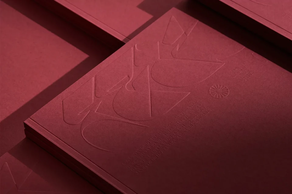 Close-up of a red book with embossed geometric designs and text, featuring a textured paper cover and minimalist design.
