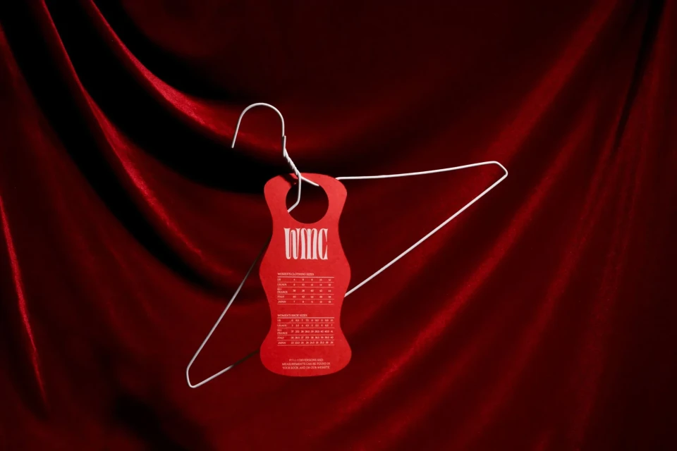 Still life of a wire hanger with a red tag on a dark red, draped fabric background, creating a minimalist and fashion-forward image.