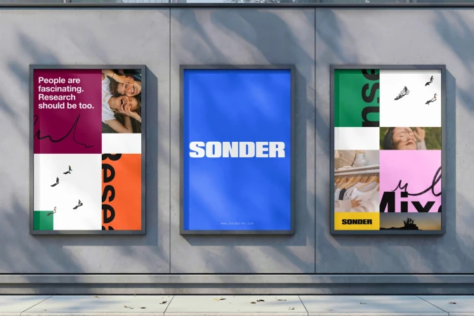 Three grey-framed posters hang on a grey wall, each featuring block color, text, and photographic collage design elements.