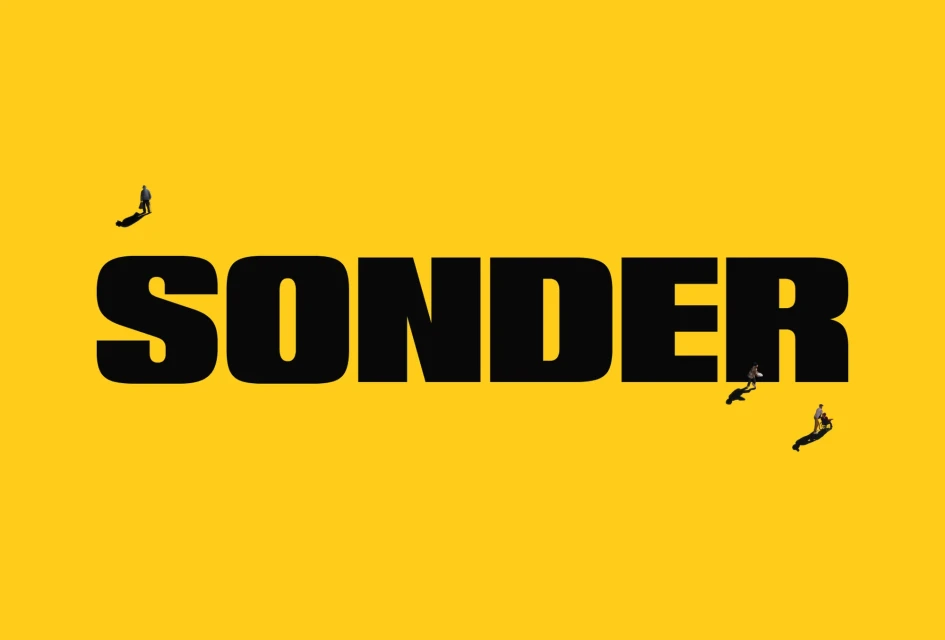 Typographic art with 'SONDER' in bold black letters against yellow. Three small figures add depth, walking along the text.