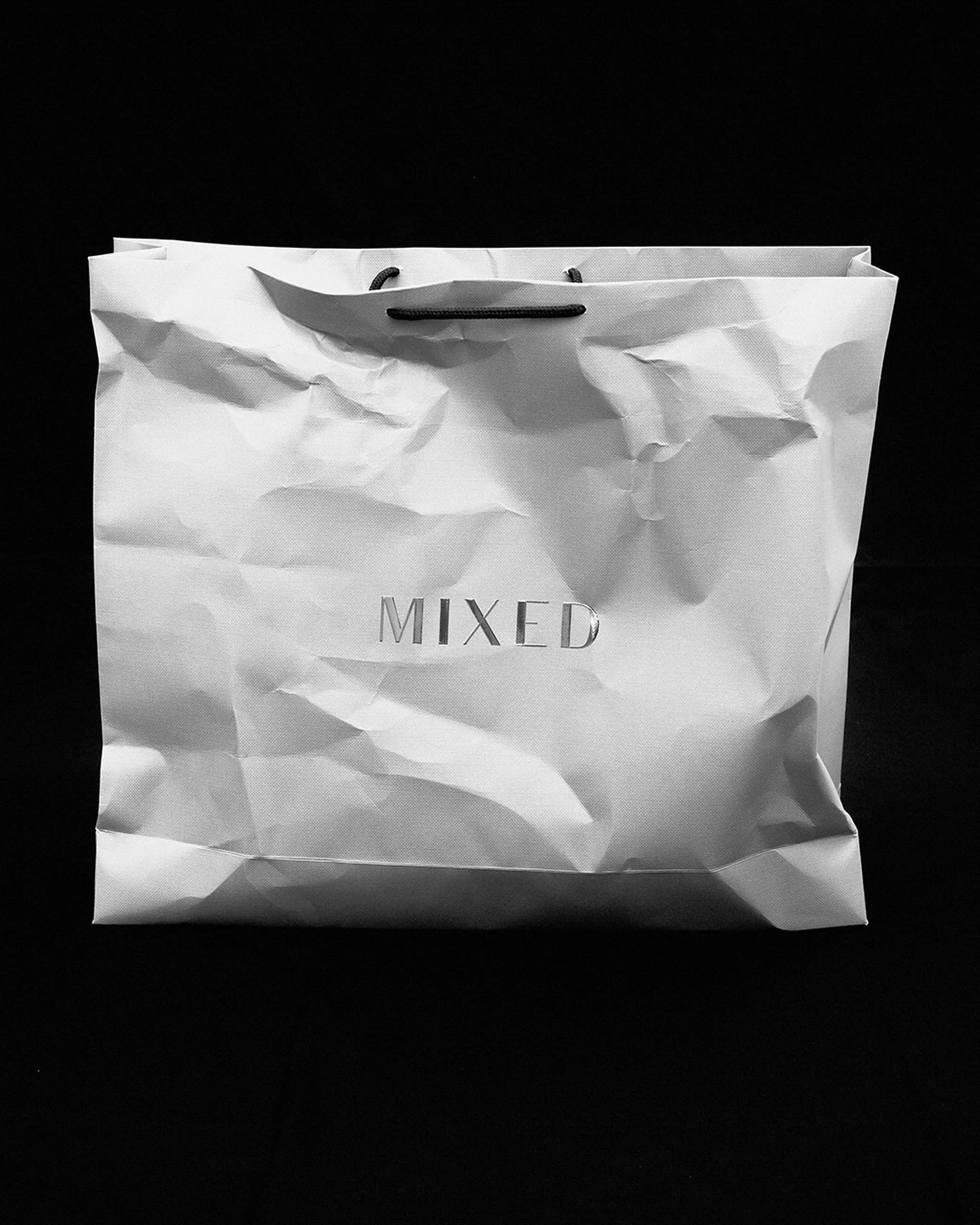 Minimalist shot of a crumpled white shopping bag with the word 'MIXED' on it against a stark black background, conveying a sense of simplicity.
