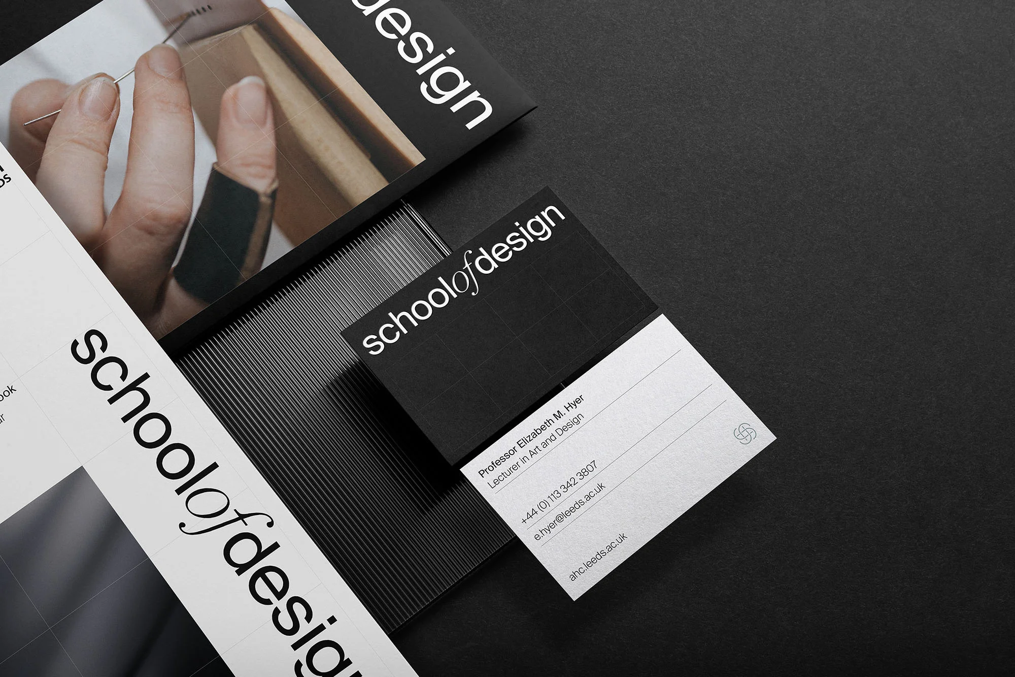 Promotional display featuring School of Design materials, including business cards, on a sleek black surface. Branding and academia focus.