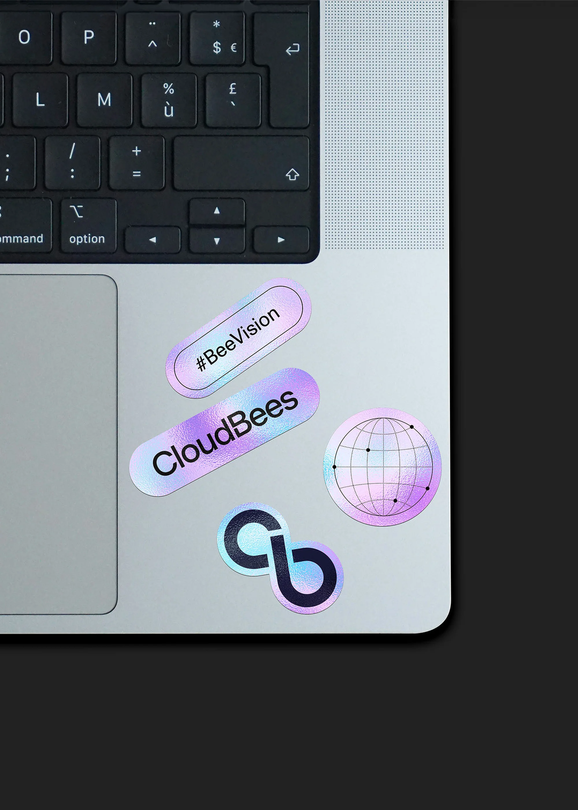 Overhead shot of a laptop with a keyboard and trackpad featuring colorful stickers, set against a dark background.