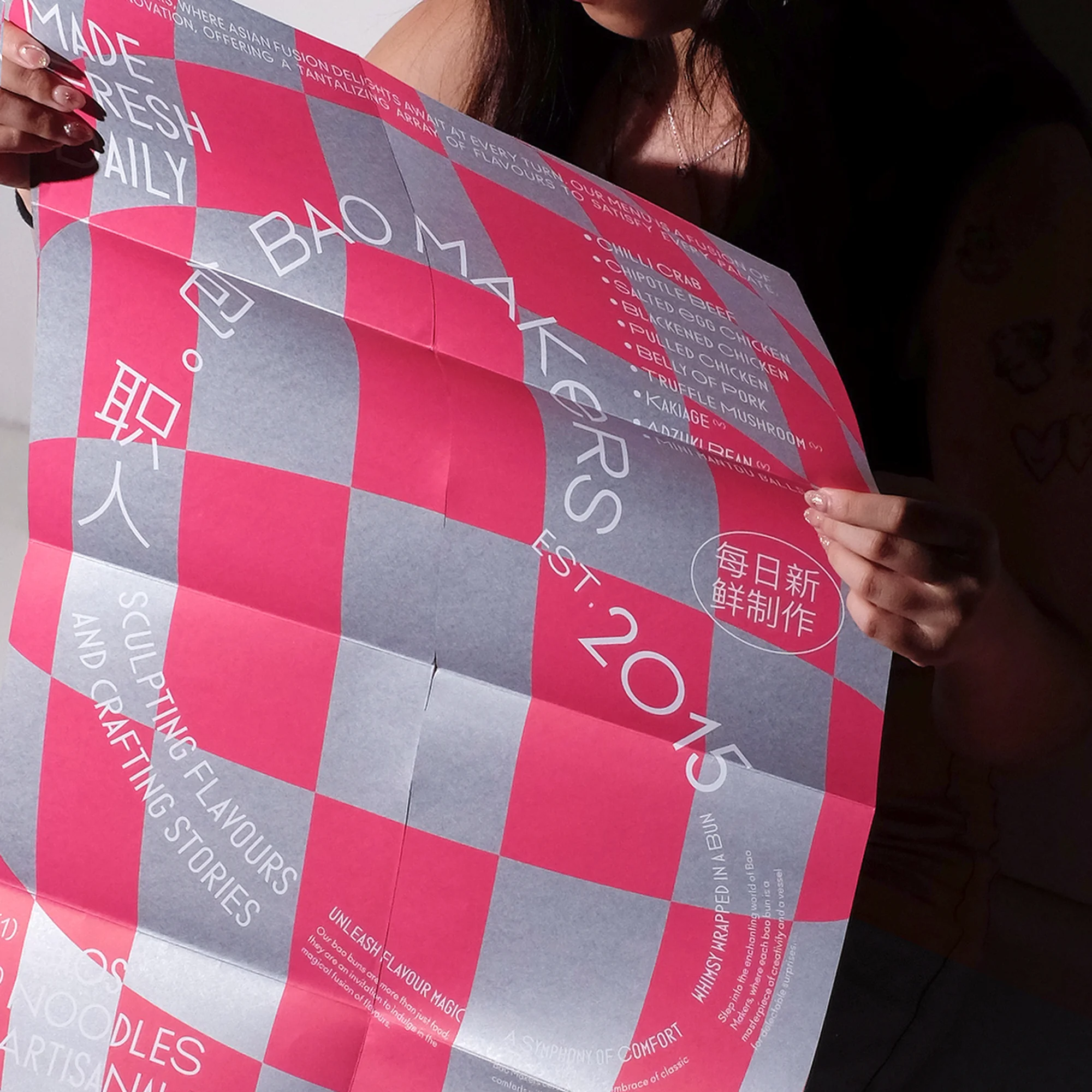 Woman holds a pink and gray checkered food poster featuring text: Bao Makers Est. 2015, fresh ingredients, and sculpting flavors stories.
