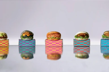 Five gourmet bao buns on colourful patterned boxes reflecting on a polished metallic surface against a clean white background