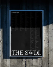 Black poster with white typography reading THE SWDL mounted on a weathered concrete wall in daylight