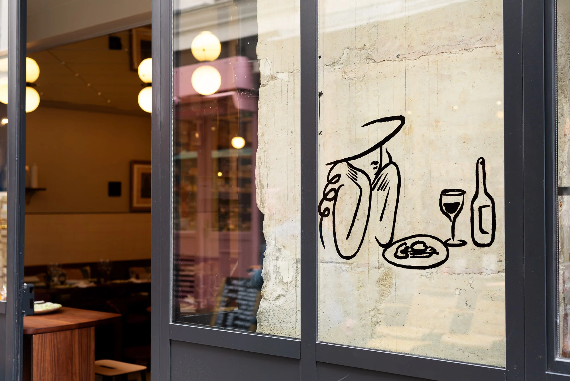 Restaurant window graphic: Woman in hat, wine bottle and glass, and food plate art on window of restaurant reflecting the interior.