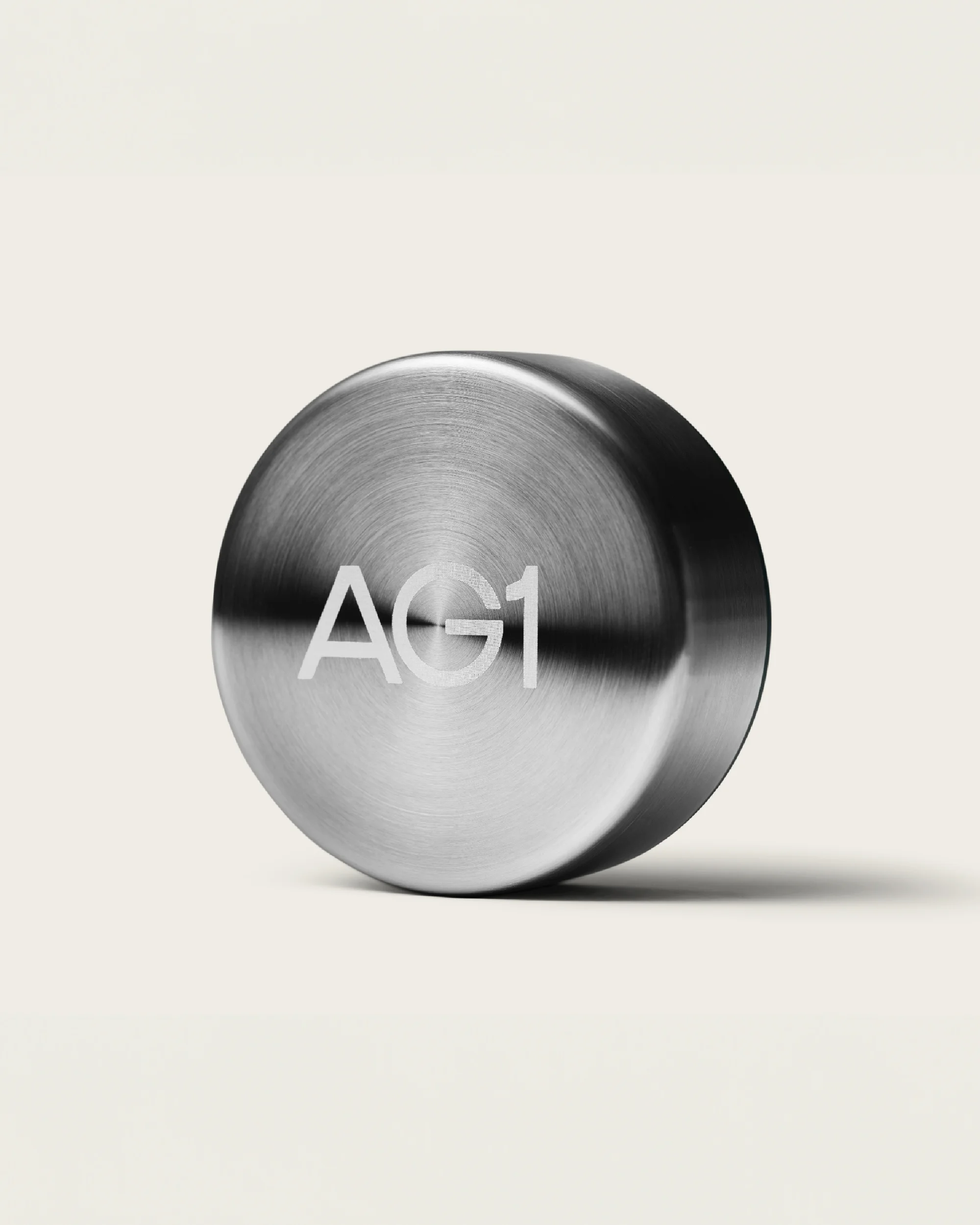 Close-up of a silver metal container featuring the white 'AG1' logo, set against a soft, neutral backdrop.