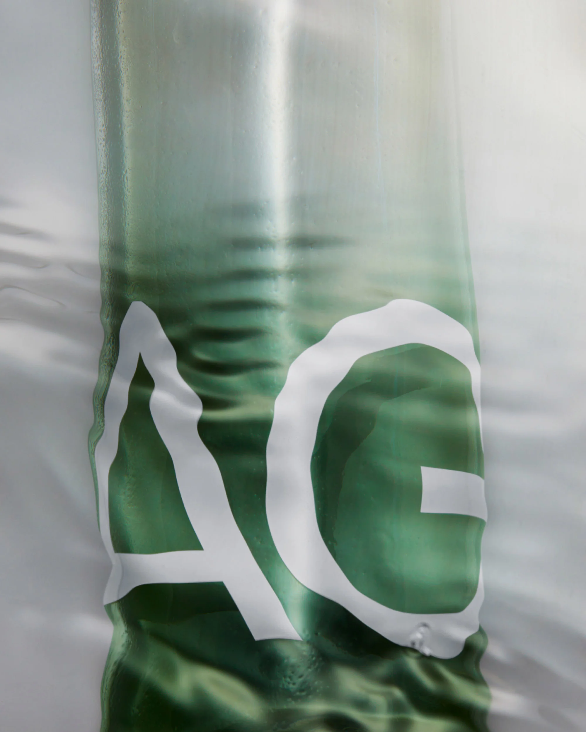 Abstract background of green liquid with subtle ripples, overlaid with a large white 'AG' logo, creating a textured, modern design.