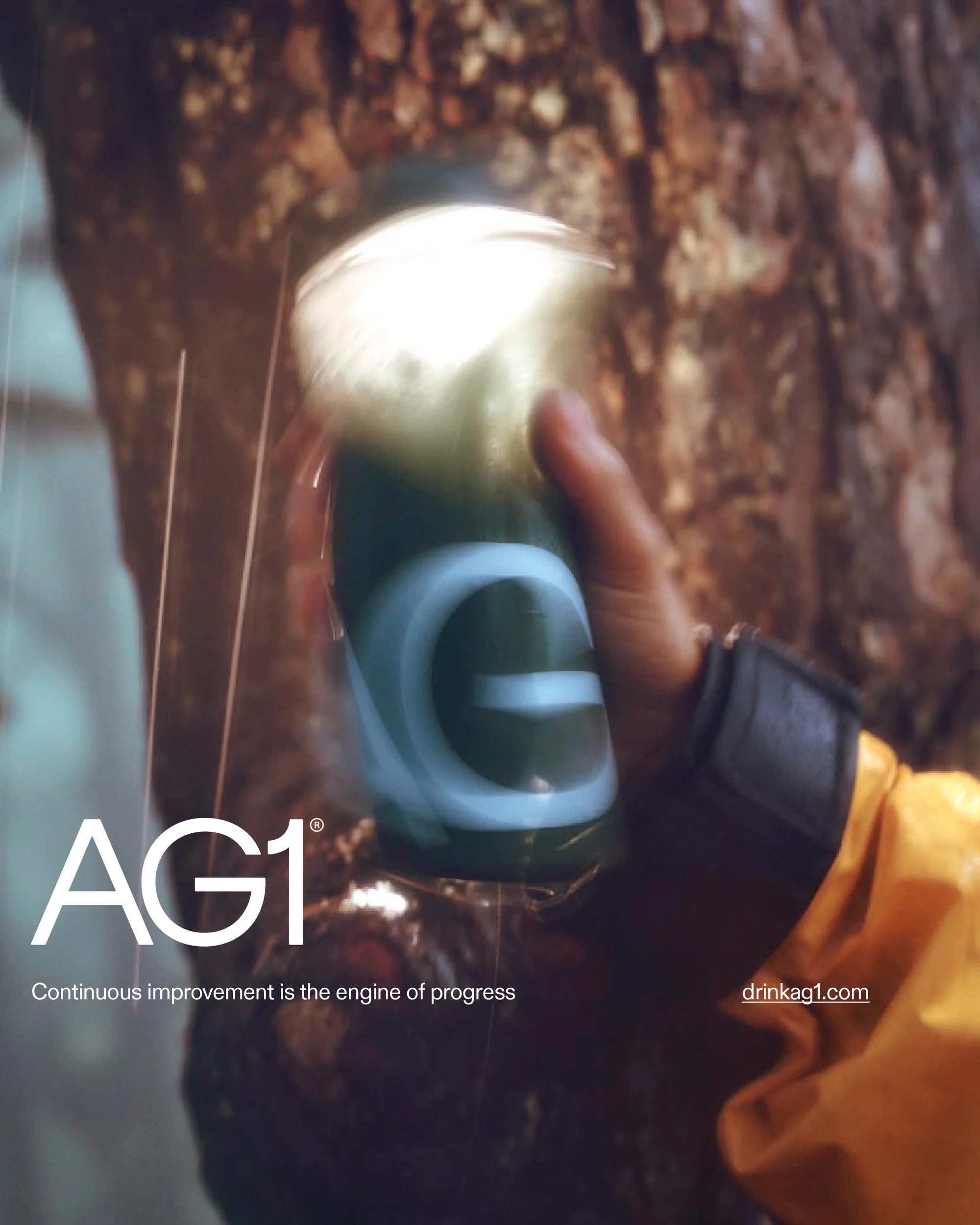 Hand holding a green drink with the letter G in front of a natural rock formation. The text AG1 and drinkag1.com are visible.