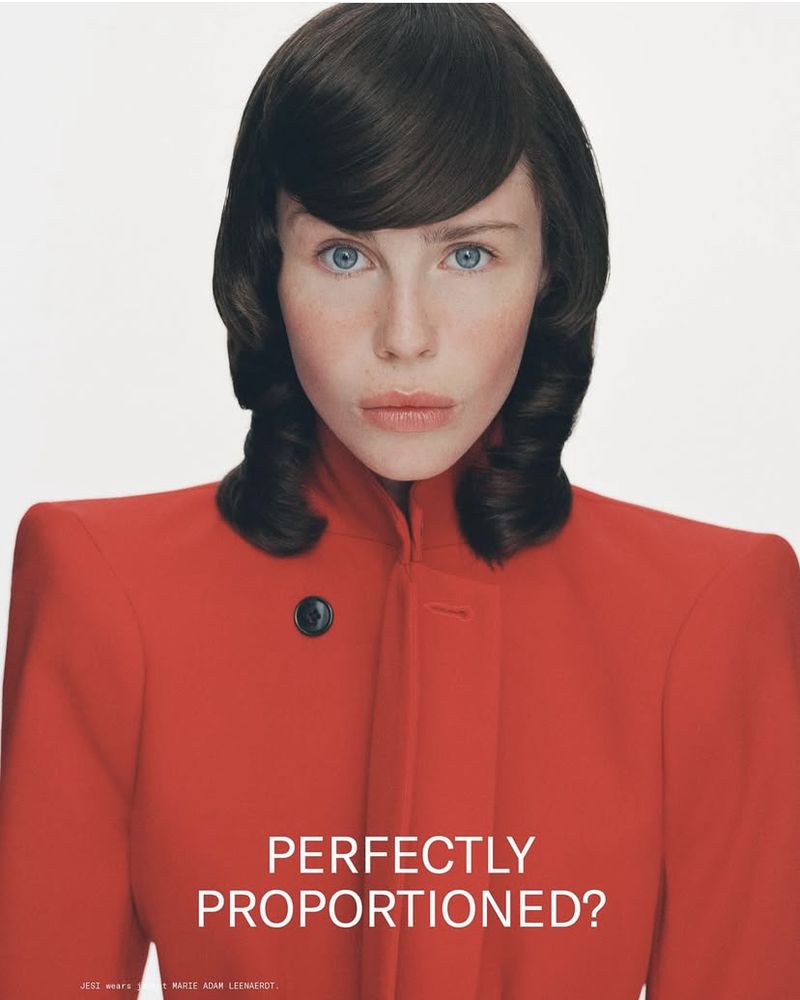 Close-up portrait of a young adult female with blue eyes and brown hair, wearing a red jacket against a clean white background.
