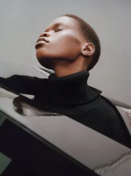 Low angle portrait of a black woman wearing a black turtleneck sweater against a plain grey background