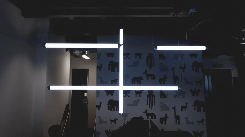 Indoor shot showcases an illuminated modern geometric light fixture with fluorescent tube lights against a wall featuring animal pattern wallpaper.