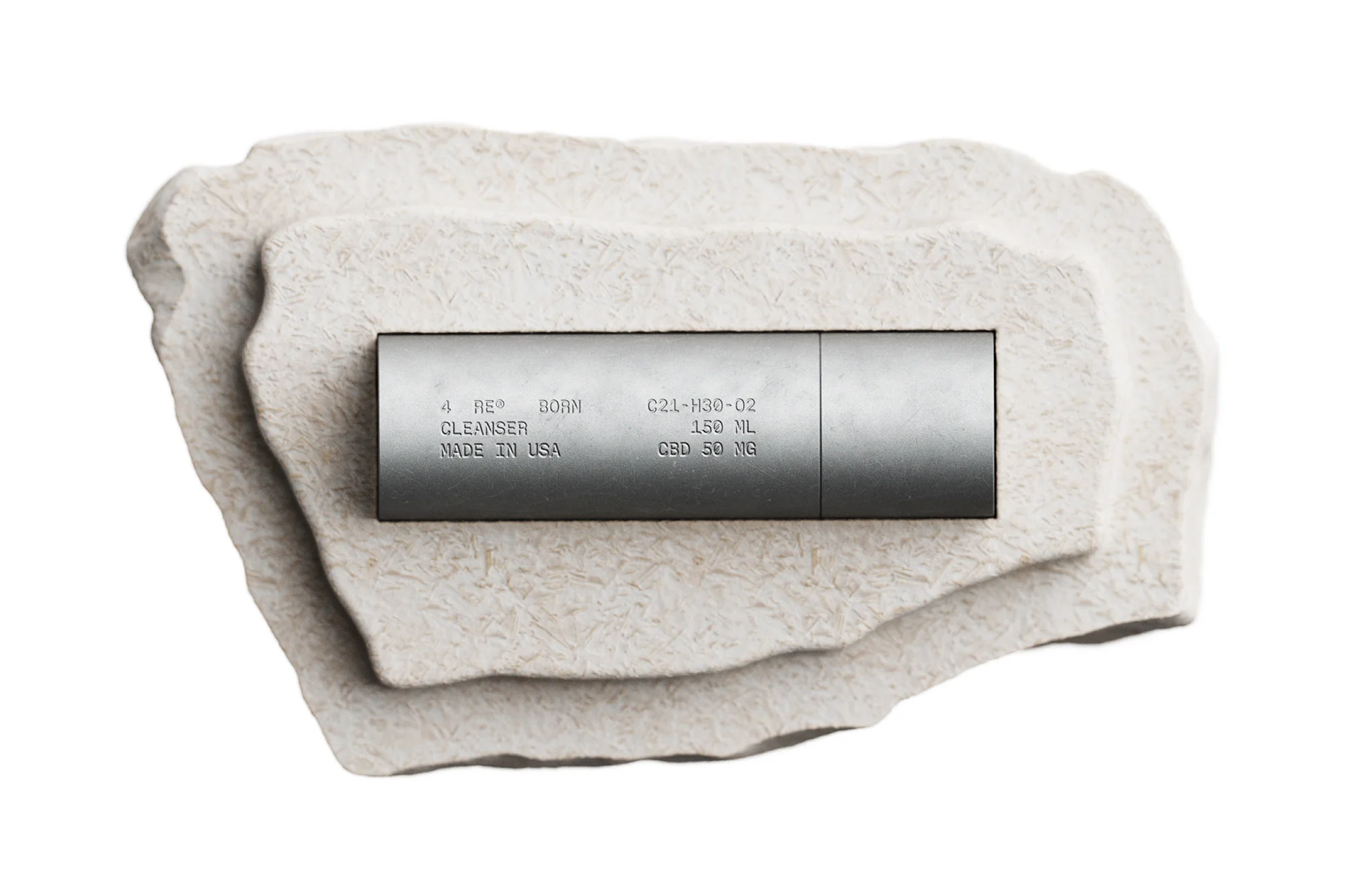 Silver cosmetic cleanser tube sits centered on a layered beige stone platform against an isolated white background in a studio shot.