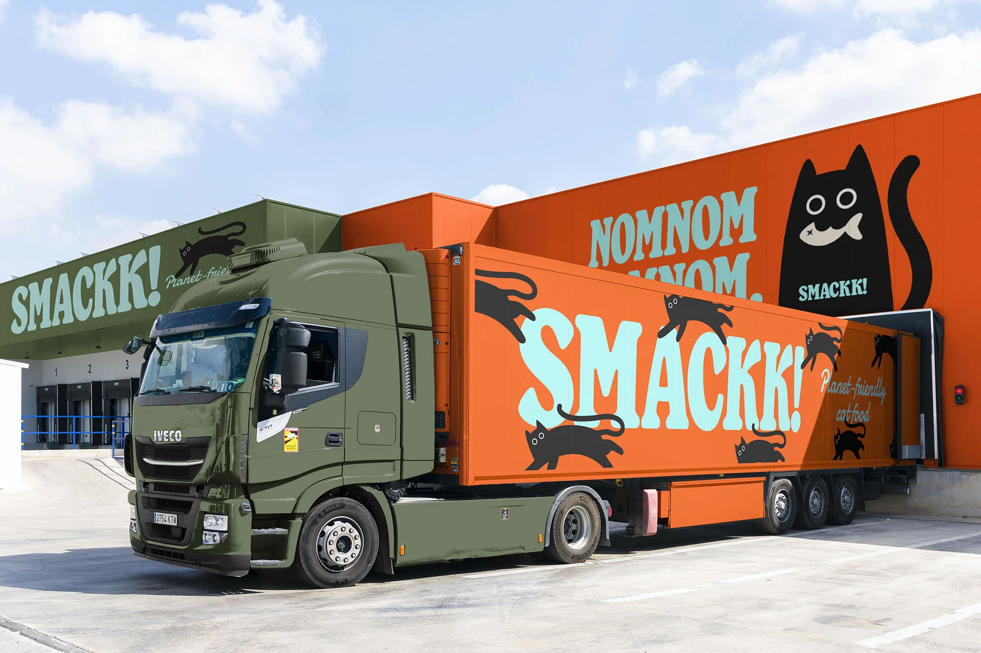 Olive green Iveco semi-truck with an orange trailer featuring 'SMACKK!' and black cat graphics, parked in front of a warehouse with branding.