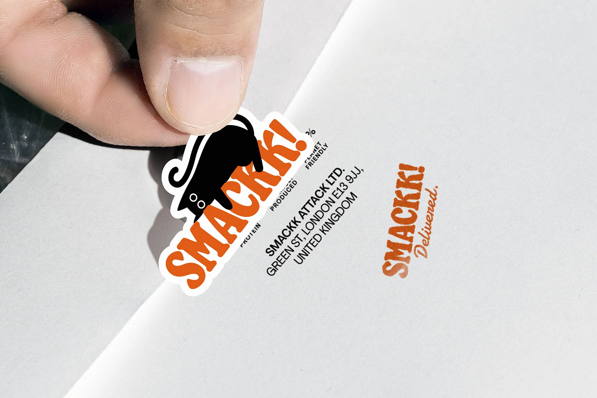 Close-up shot of a hand holding a sticker with a cartoon black cat and the brand name "Smackk!" in orange lettering.