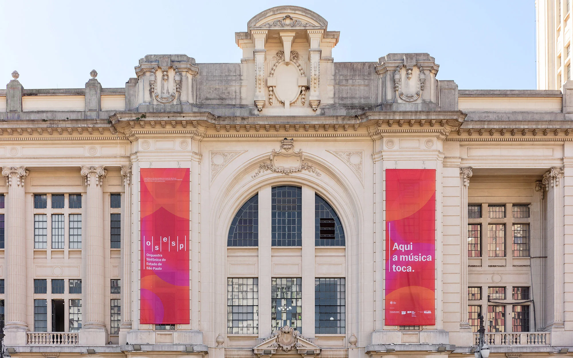 Exterior of Theatro Municipal in São Paulo, Brazil featuring banners with text in Portuguese and a classical architectural style.