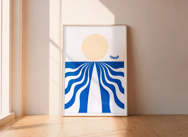 Framed graphic art print features blue and white wavy lines converging below a yellow sun, displayed in minimalist room setting.